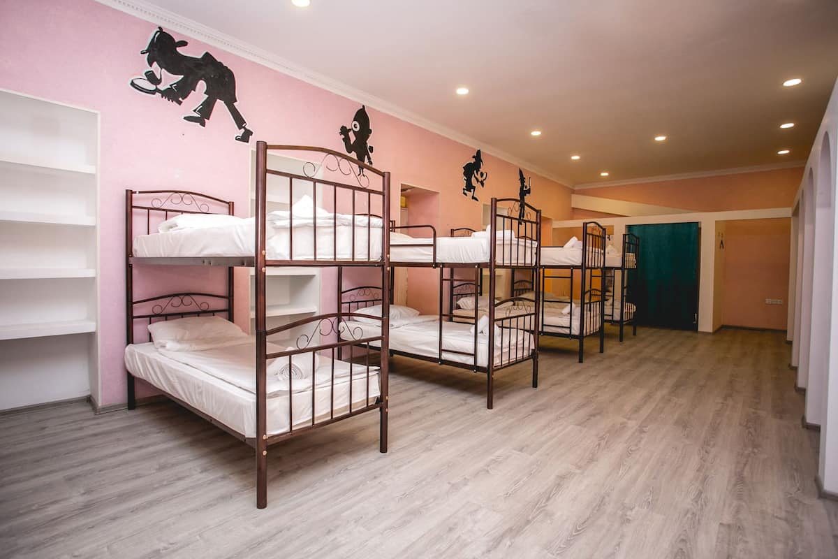 A dormitory room with bunk beds, pink walls, and a wooden floor.