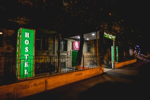 A hostel with a green signboard, a small entrance, and a staircase leading up to the door.