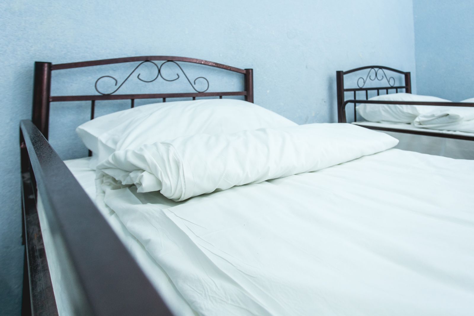 Un lit simple avec un matelas et un oreiller blancs, une tête de lit en bois et un mur bleu uni.