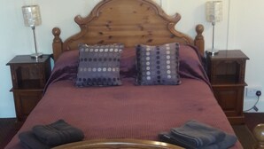 A wooden bed with a headboard, two bedside tables, and three pillows. - Tudor House (Wisbech)