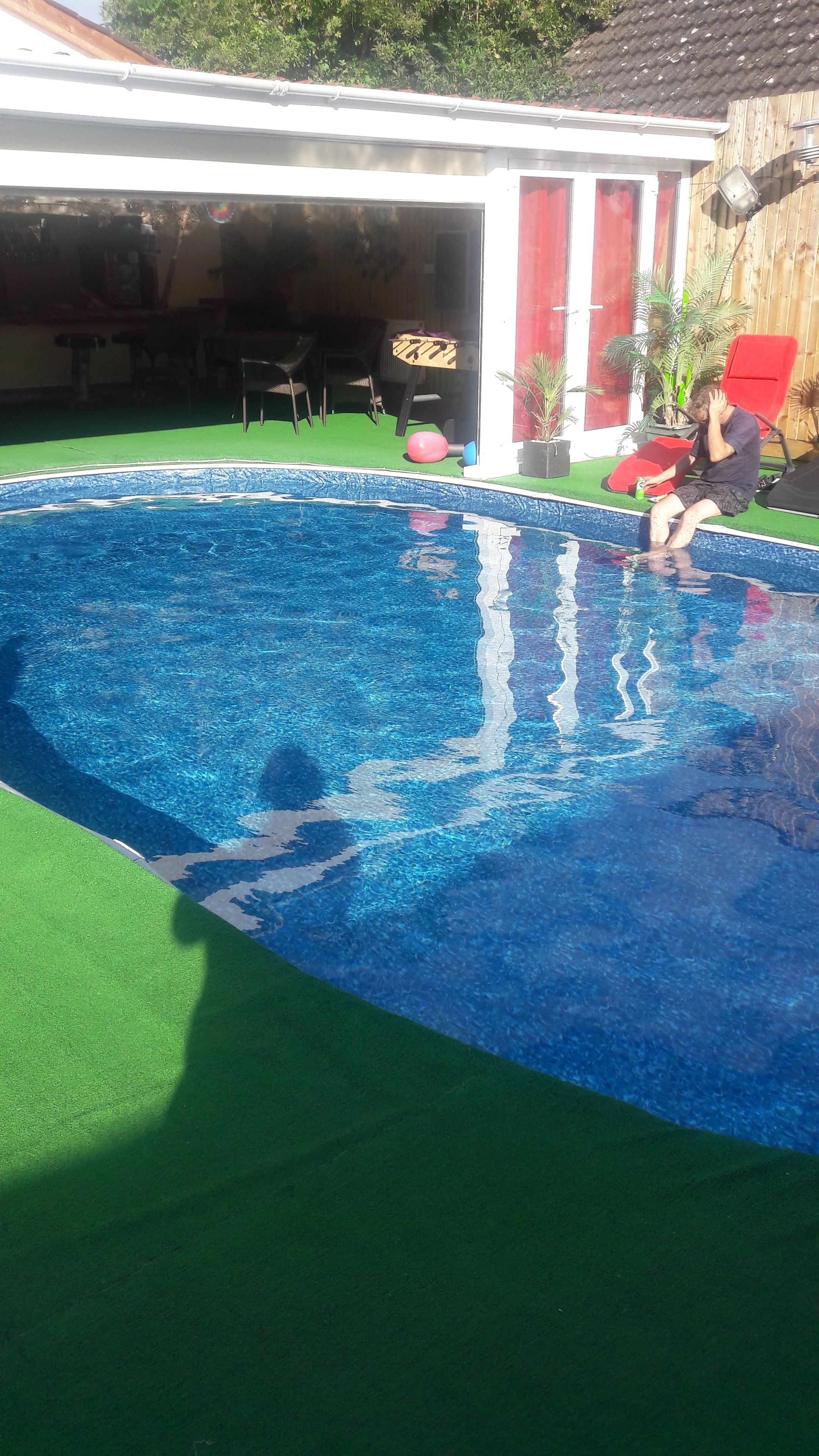 Piscina com água azul cristalina, rodeada por uma área de grama sintética verde.