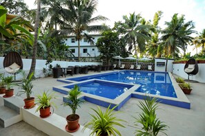 A swimming pool with a tiled deck, surrounded by potted plants and palm trees. - Amara Grand Baga (Baga)