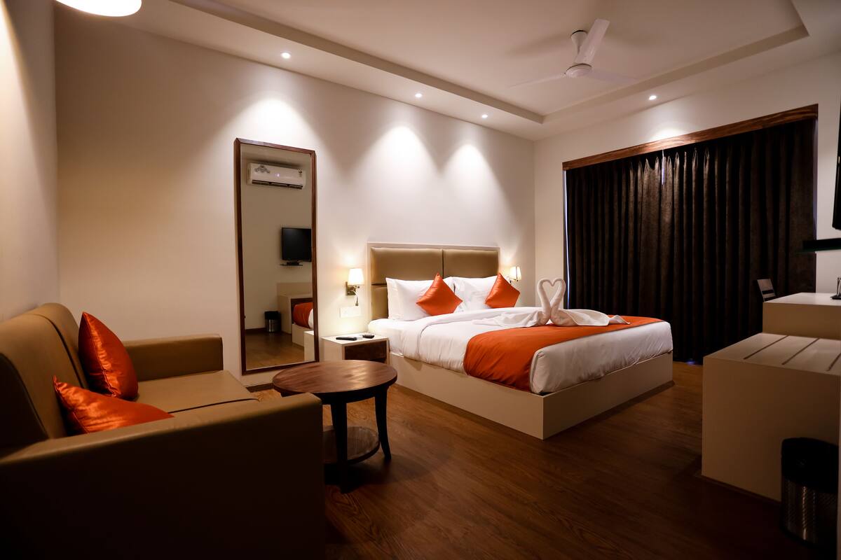 Una habitación de hotel moderna con una cama grande, un sofá, una mesita y un espejo.