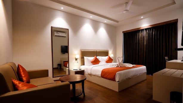 A modern hotel room with a large bed, a sofa, a small table, and a mirror. - Amara Grand Baga (Baga)