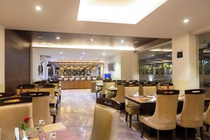 A modern restaurant with a central bar, multiple dining tables, and comfortable seating. - Amara Grand Baga (Baga)