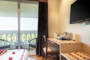 A hotel room with a bed, a desk, a chair, a television, and a balcony with wicker furniture. - Amara Grand Baga (Baga)