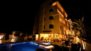 A hotel with a swimming pool, outdoor seating, and a well-lit facade at night. - Amara Grand Baga (Baga)
