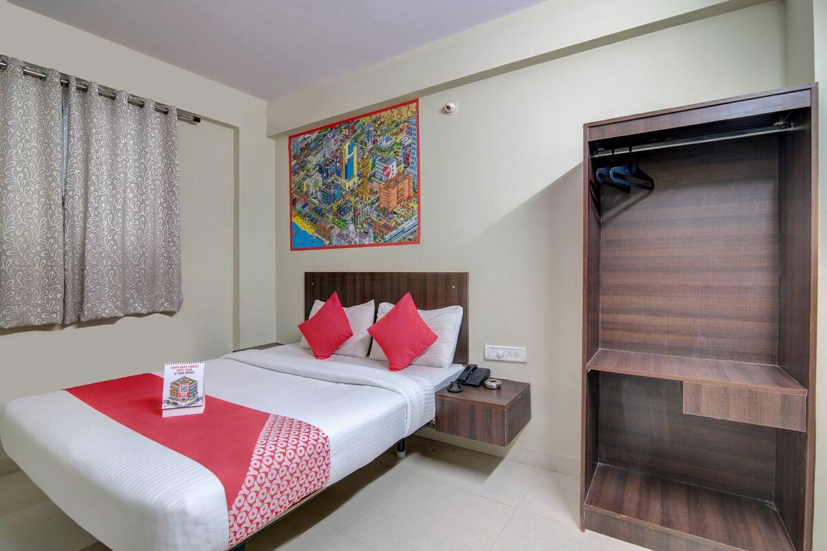 Une chambre d’hôtel avec un lit, une table de chevet, une armoire en bois et une œuvre d’art colorée représentant un paysage urbain accrochée au mur.