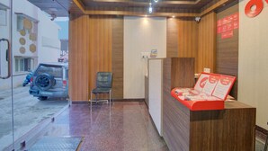 A reception area with a wooden reception desk, a chair, and a car parked outside. - OYO 11916 Varcity Plaza (Bengaluru)