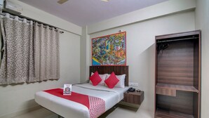 A hotel room with a bed, a nightstand, a wooden wardrobe, a painting on the wall, and a window with curtains. - OYO 11916 Varcity Plaza (Bengaluru)