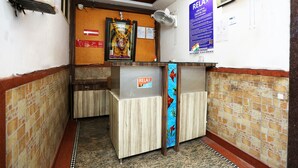 A reception area with a wooden reception desk, a wall-mounted fan, and a poster advertising a service. - OYO 12682 Hotel Relax (Gwalior)