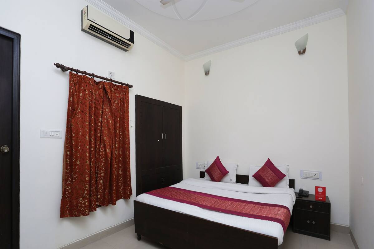 A bedroom with a bed, a wardrobe, a nightstand, an air conditioner, and a curtain.