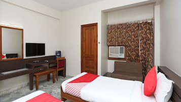 A hotel room with two beds, a desk, a television, a wardrobe, and an air conditioning unit.