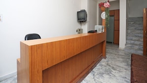 A reception desk with a flat-screen TV, a telephone, and a small plant. There is a staircase leading to an upper level. - OYO 14577 Vijay Palace (Bhopal)