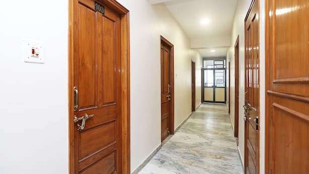A hallway with wooden doors, a marble floor, and a light switch on the wall. - OYO 14577 Vijay Palace (Bhopal)