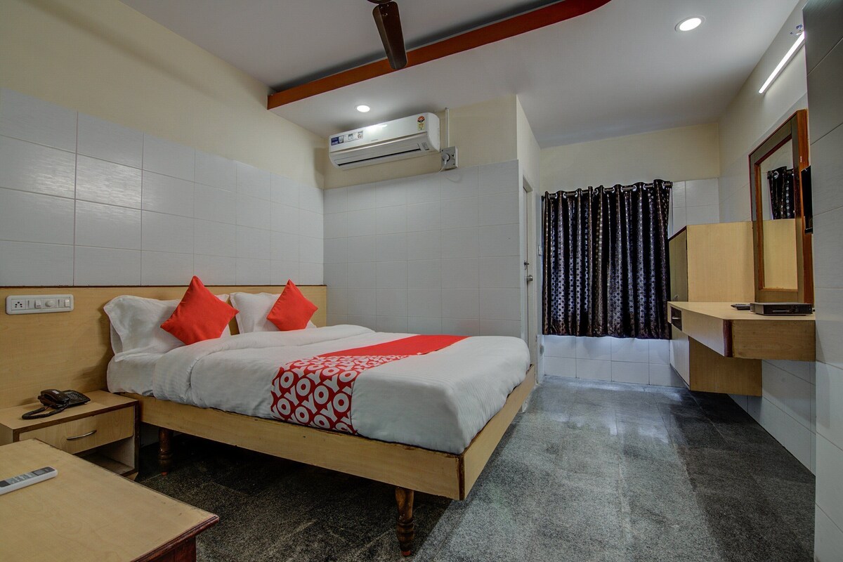 A hotel room with a bed, bedside table, nightstand, and a small desk with a chair.
