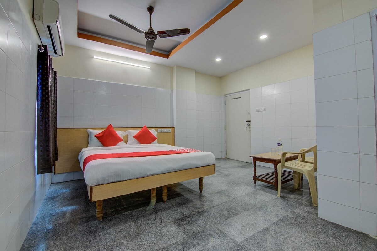 A hotel room with a bed, a ceiling fan, a table with a chair, and a water bottle on the table.