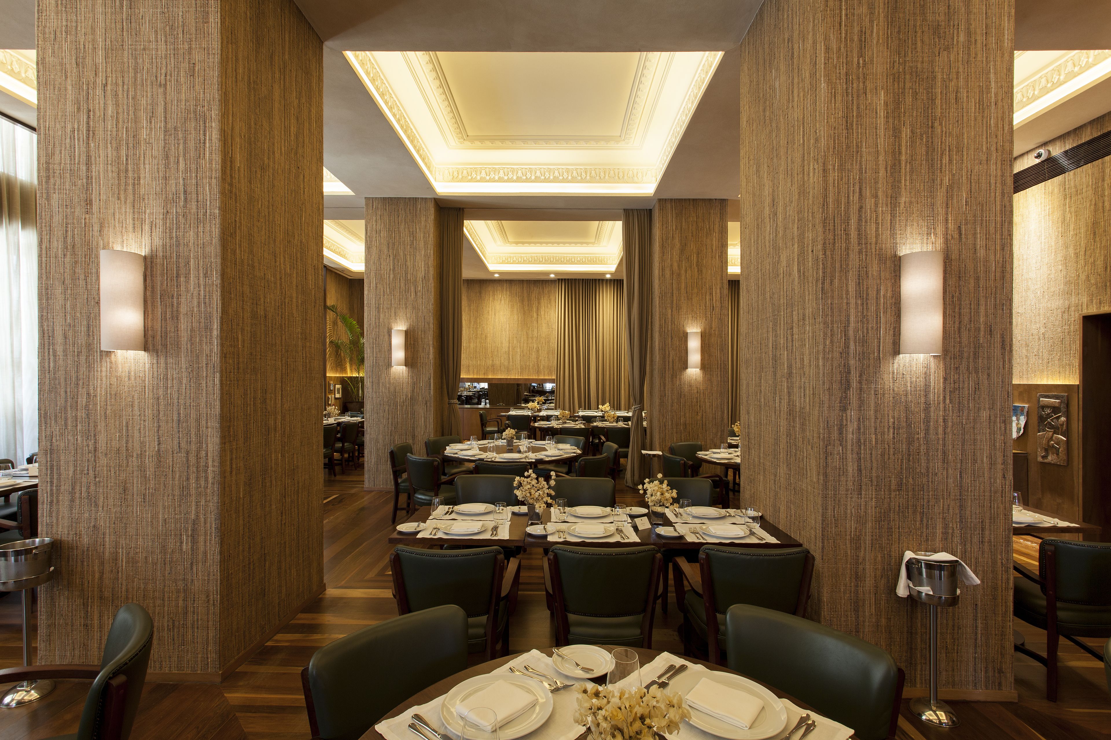 Un vaste espace dédié à la salle à manger, avec plusieurs tables dressées, présentant un design moderne avec des panneaux en bois et un éclairage encastré.