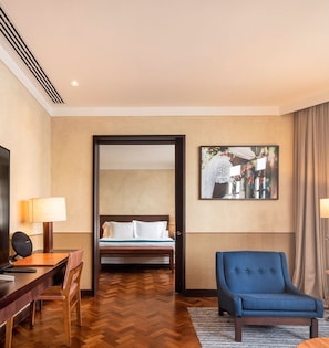 Una habitación de hotel con cama, escritorio con lámpara, silla y sillón azul.