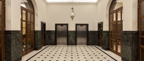 A lobby with a marble floor, two elevators, and wooden doors.