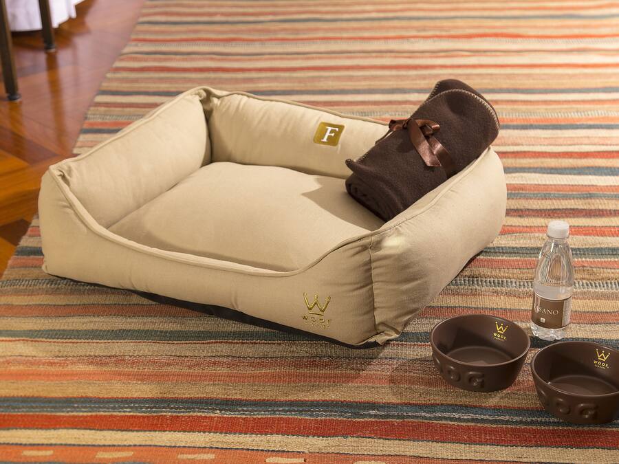 Un panier pour animal de compagnie avec un coussin marron et deux gamelles posées sur un tapis à rayures.