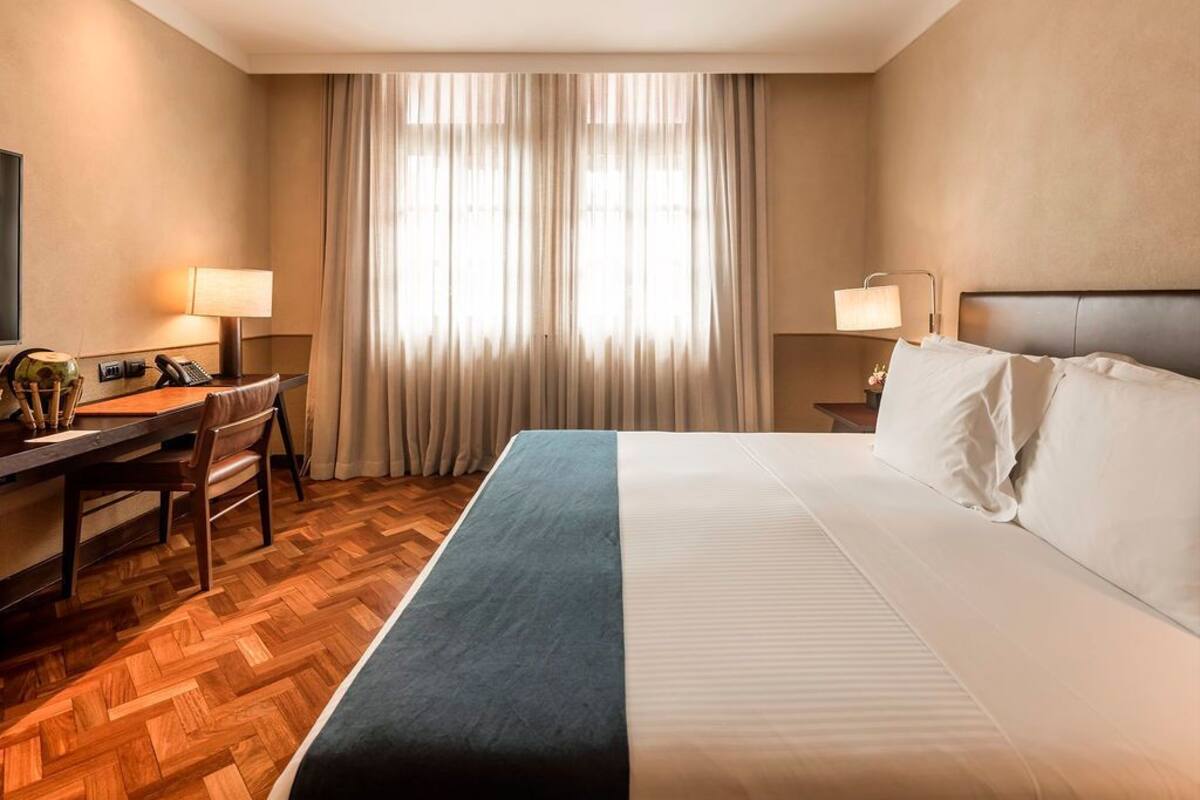 Ein Hotelzimmer mit Bett, Schreibtisch mit Stuhl, Fernseher und einem Fenster mit Vorhängen.