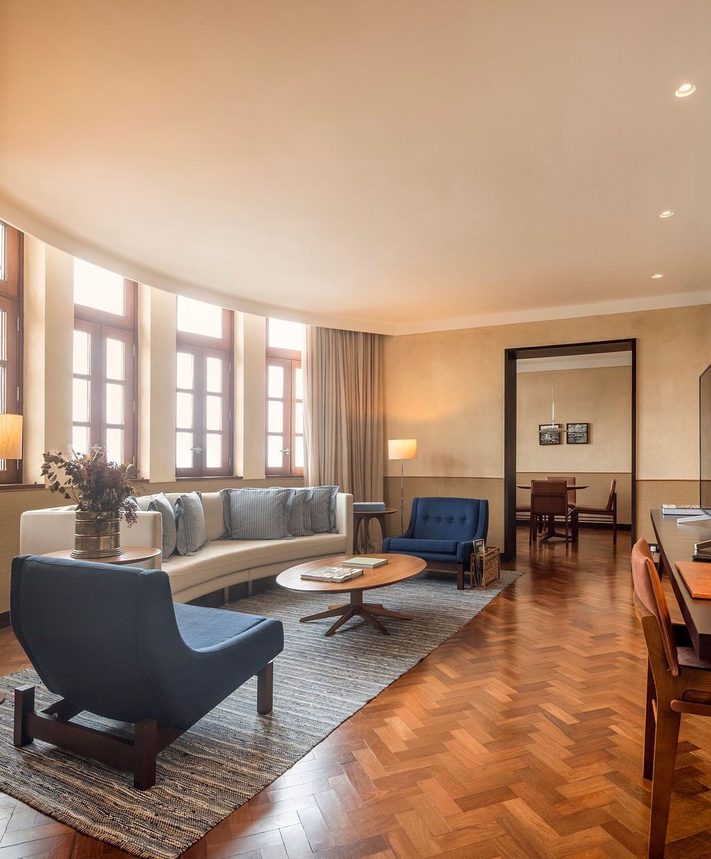 A spacious living area with a sofa, a blue armchair, a coffee table, and a dining area with chairs and a table.
