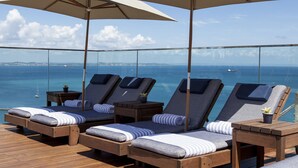 A balcony with lounge chairs and umbrellas overlooking the sea. - Hotel Fasano Salvador (Salvador)