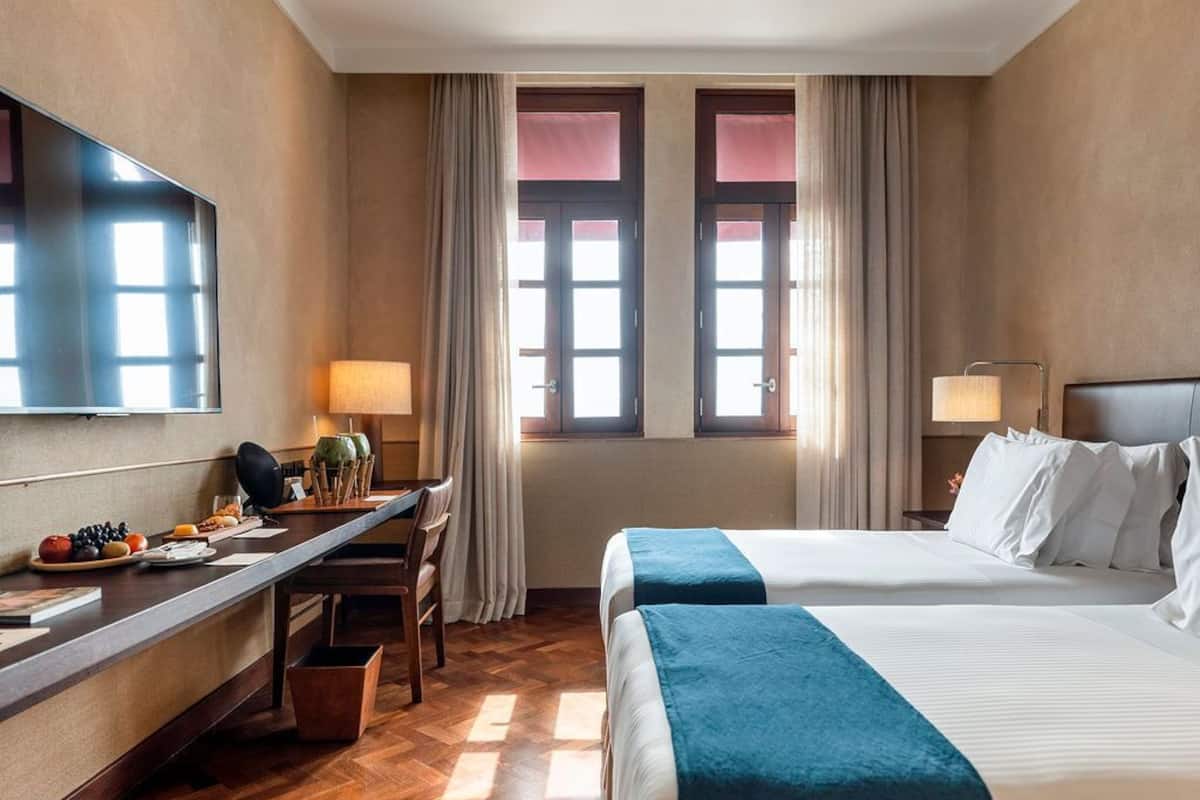 Ein Hotelzimmer mit Bett, Schreibtisch, Fernseher und einem fenster mit Vorhängen.