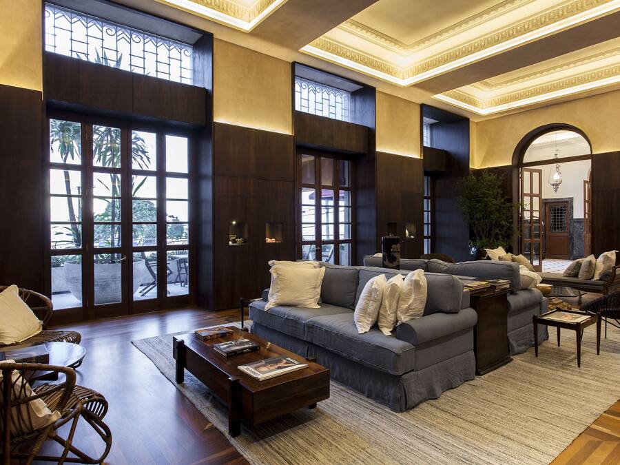 A spacious living room with a large grey sofa, a wooden coffee table, and wicker chairs.
