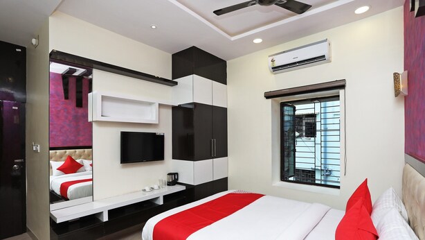 A modern bedroom with a bed, a TV, a desk, and an air conditioning unit. - OYO 15617 Abi's Inn (Kolkata)