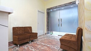 A room with a brown sofa, a white cabinet, and a large sliding door with a marble-patterned floor. - OYO 15617 Abi's Inn (Kolkata)