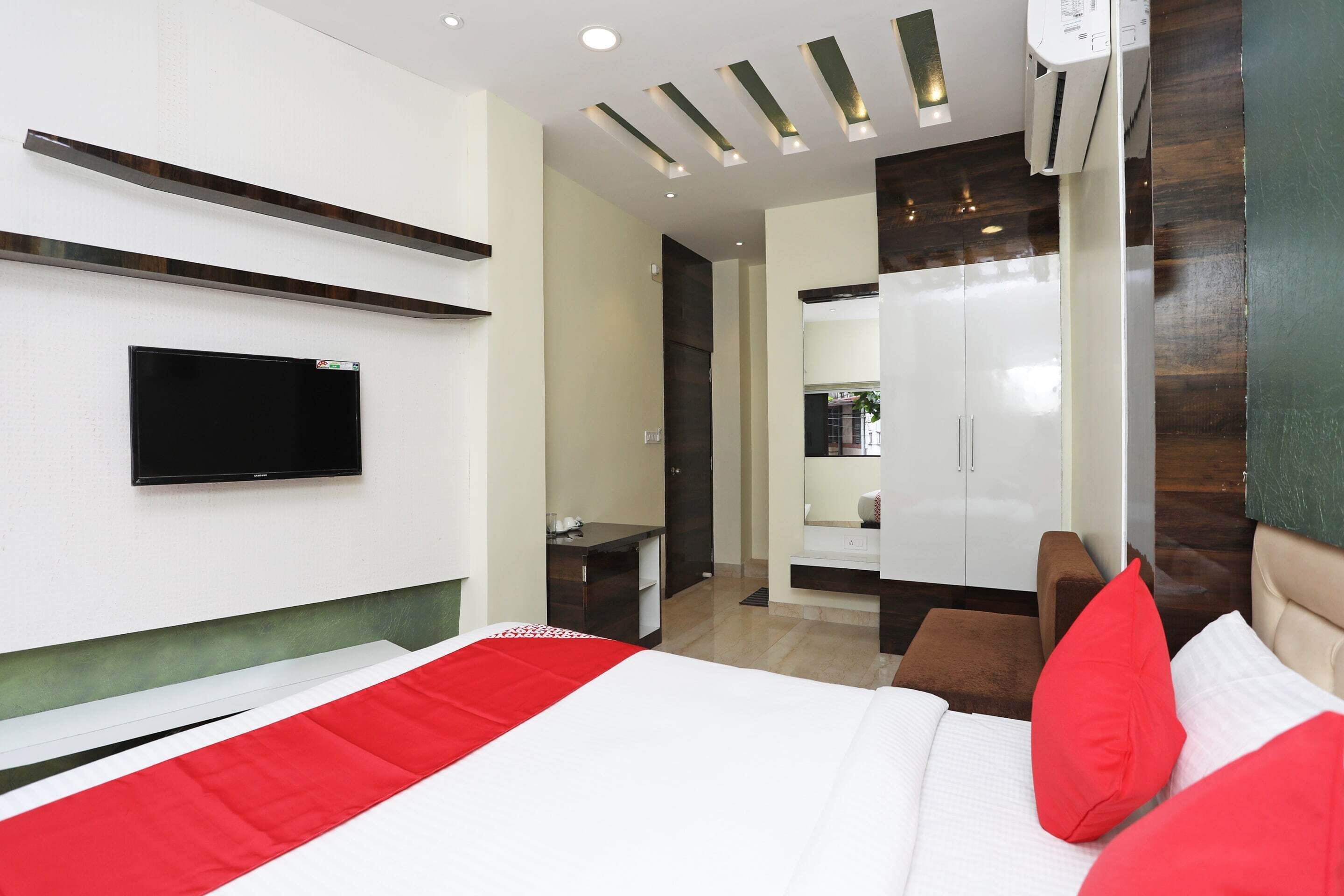 A modern hotel room with a bed, a TV mounted on the wall, a wardrobe, and a small desk.