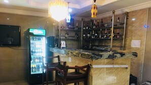 A bar area with a marble countertop, wooden chairs, a wine rack, and a television screen. - Feligold Royal Hotel Benin (Benin City)