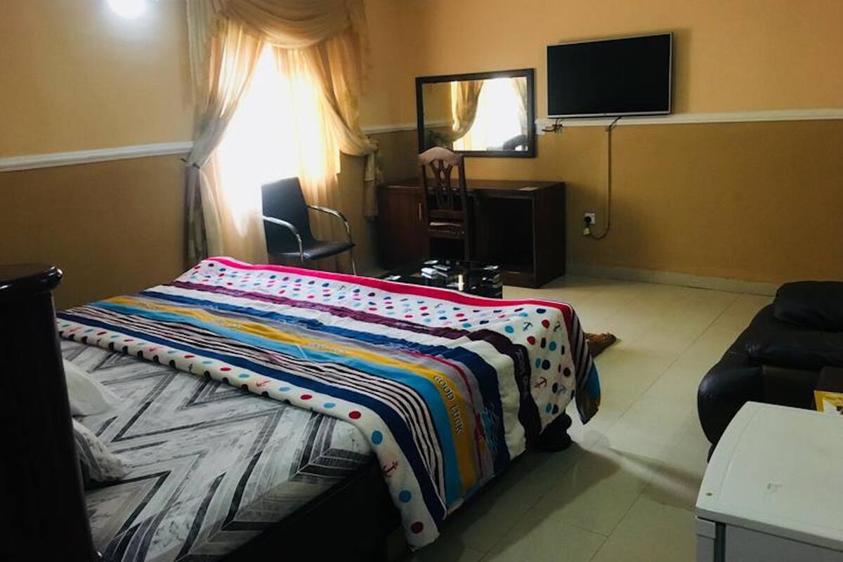 A hotel room with a bed, a desk, a chair, a television, and a wardrobe.