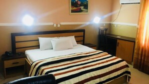 A hotel room with a bed, a nightstand, a desk, and an air conditioning unit. - Feligold Royal Hotel Benin (Benin City)