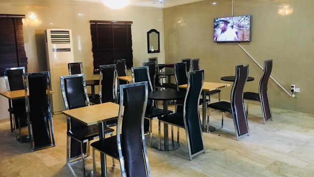 A dining area with tables and chairs, a television mounted on the wall, and an air conditioning unit. - Feligold Royal Hotel Benin (Benin City)