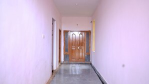 Un couloir avec une porte en bois au fond, un sol carrelé et des murs de couleur claire.