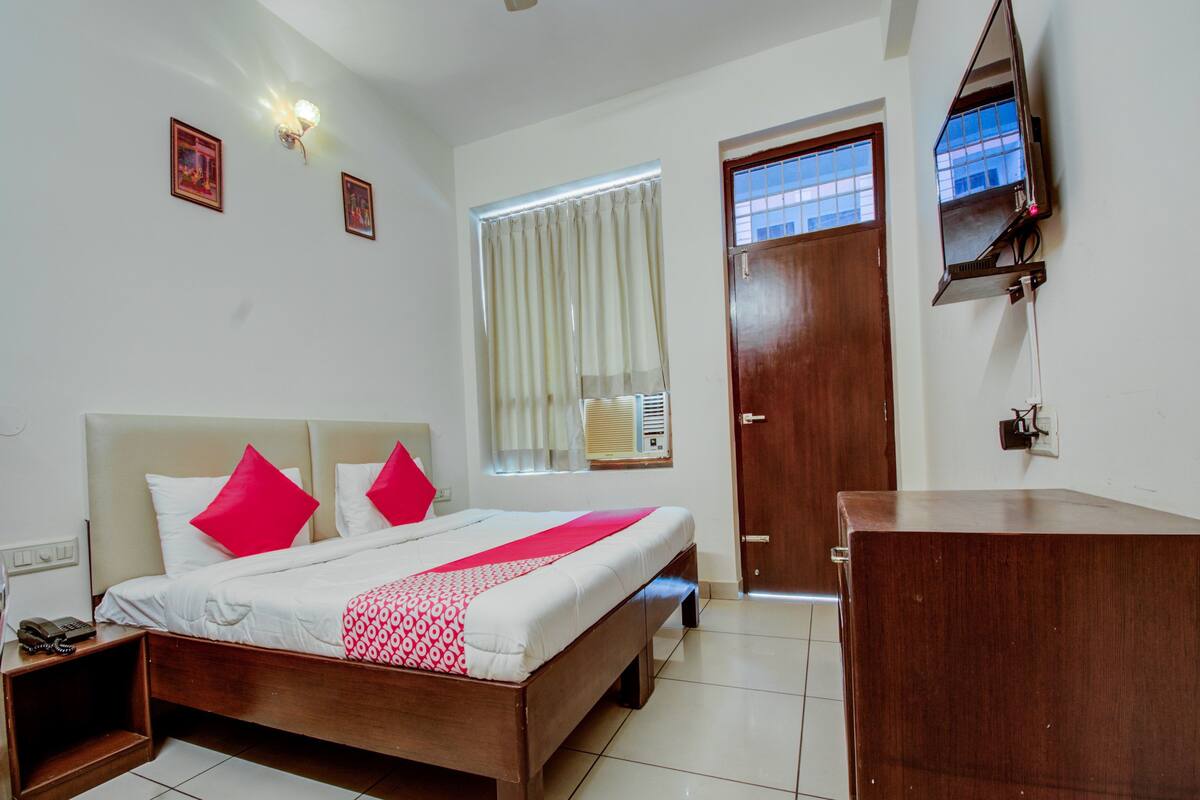 A hotel room with a bed, bedside table, and a wooden dresser.