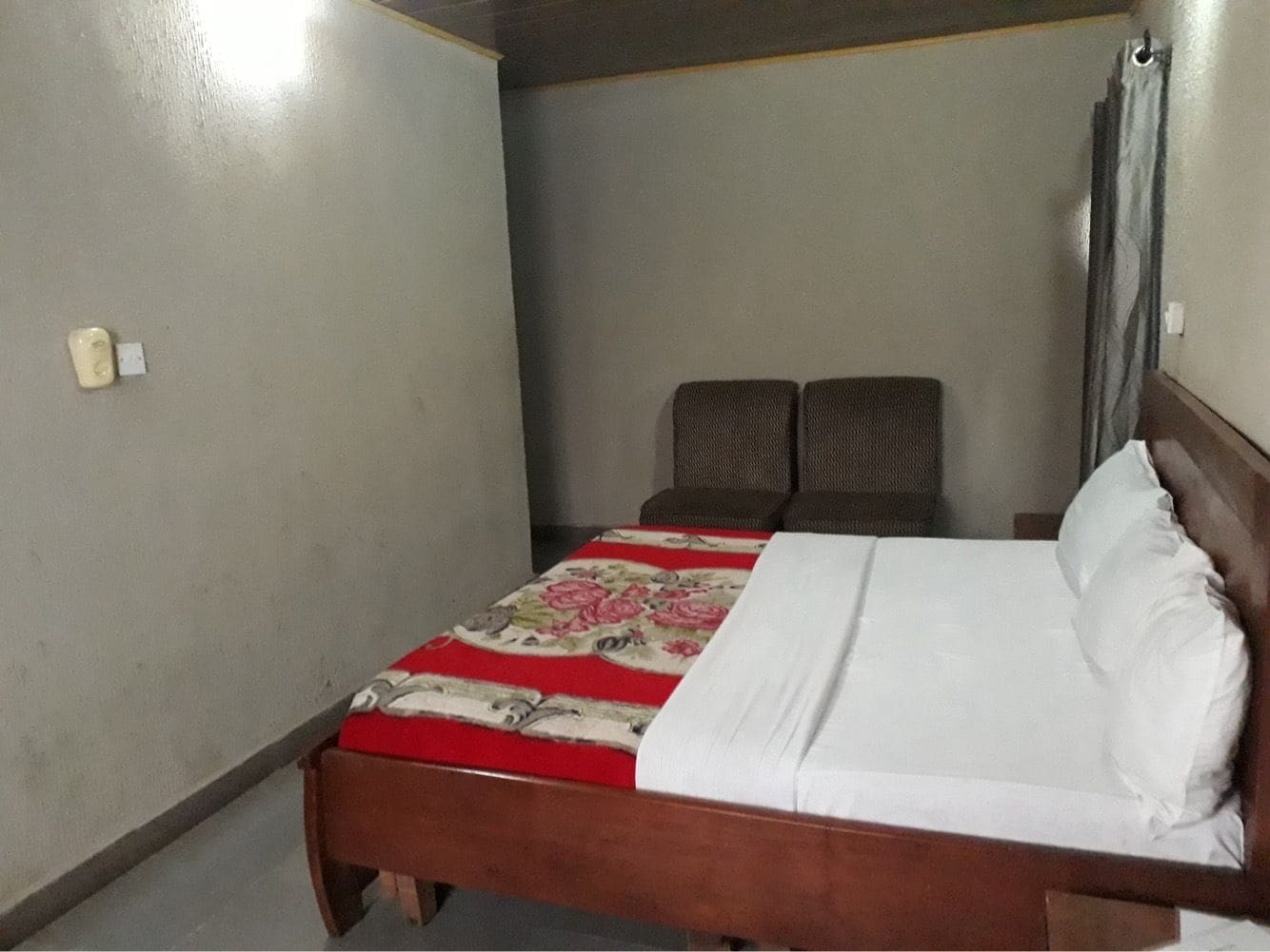 A single bed with a floral bedspread, two upholstered chairs, and a wooden headboard.
