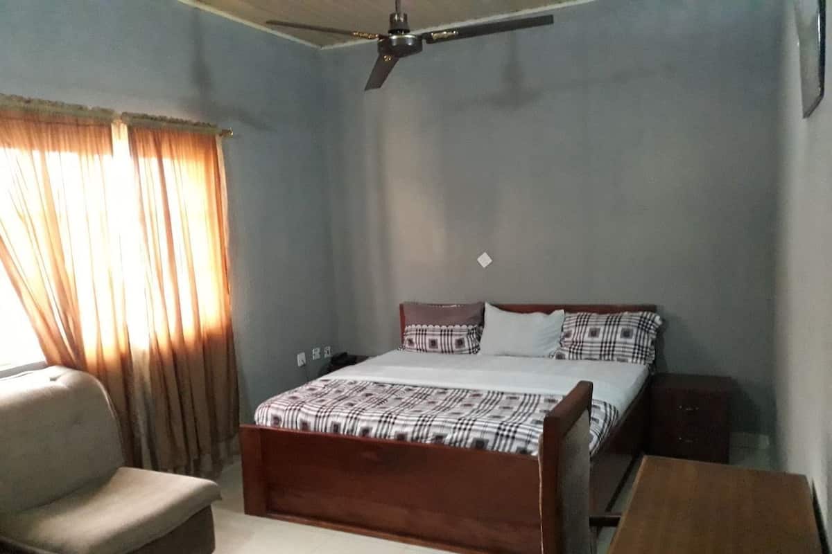 A bedroom with a bed, a chair, a bedside table, and a ceiling fan.