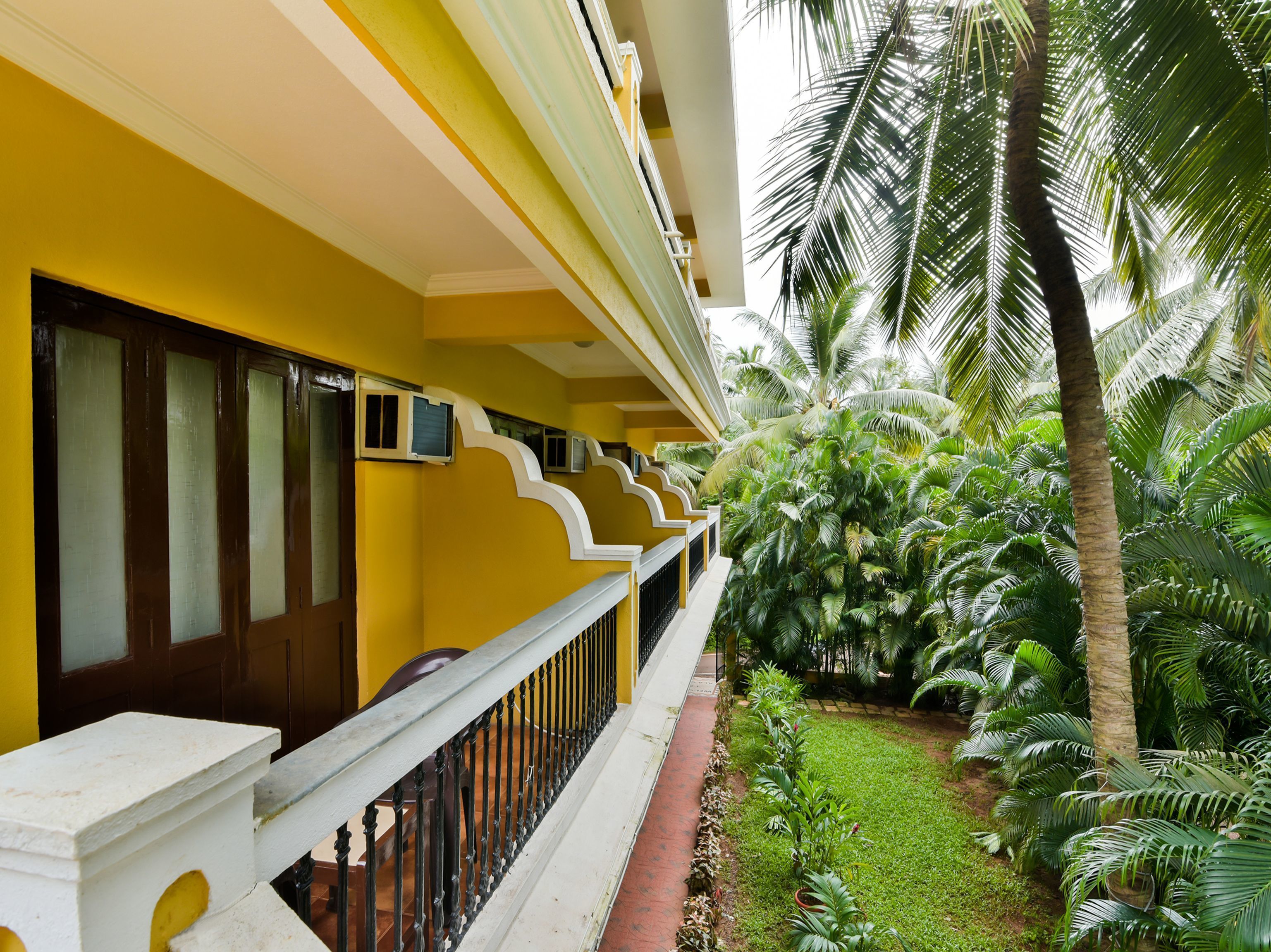 A yellow building with a balcony, surrounded by lush greenery and palm trees.