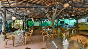 Un espace de restauration en plein air avec des chaises et des tables en bois, un toit de chaume et des luminaires suspendus.