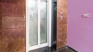 Un couloir aux murs de marbre et une porte en verre donnant sur un ascenseur.