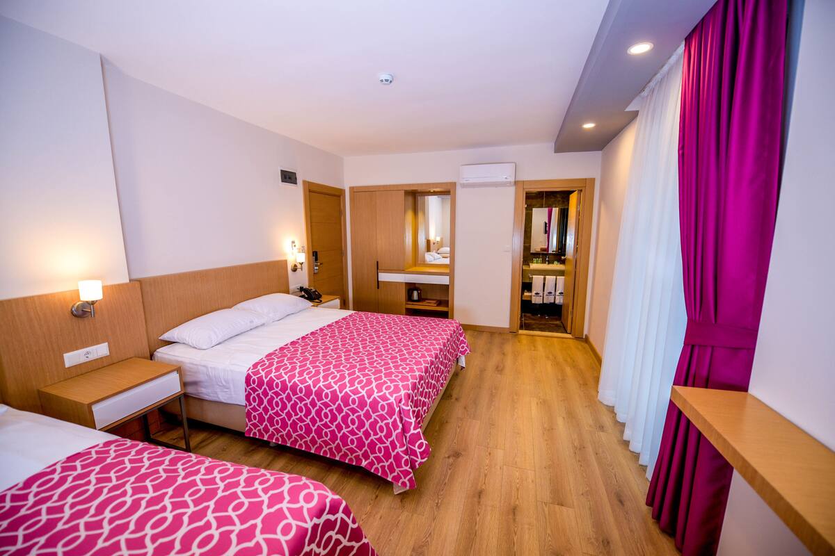 Une chambre d’hôtel avec deux lits, un plancher en bois, une salle de bain avec un miroir et une fenêtre avec des rideaux.