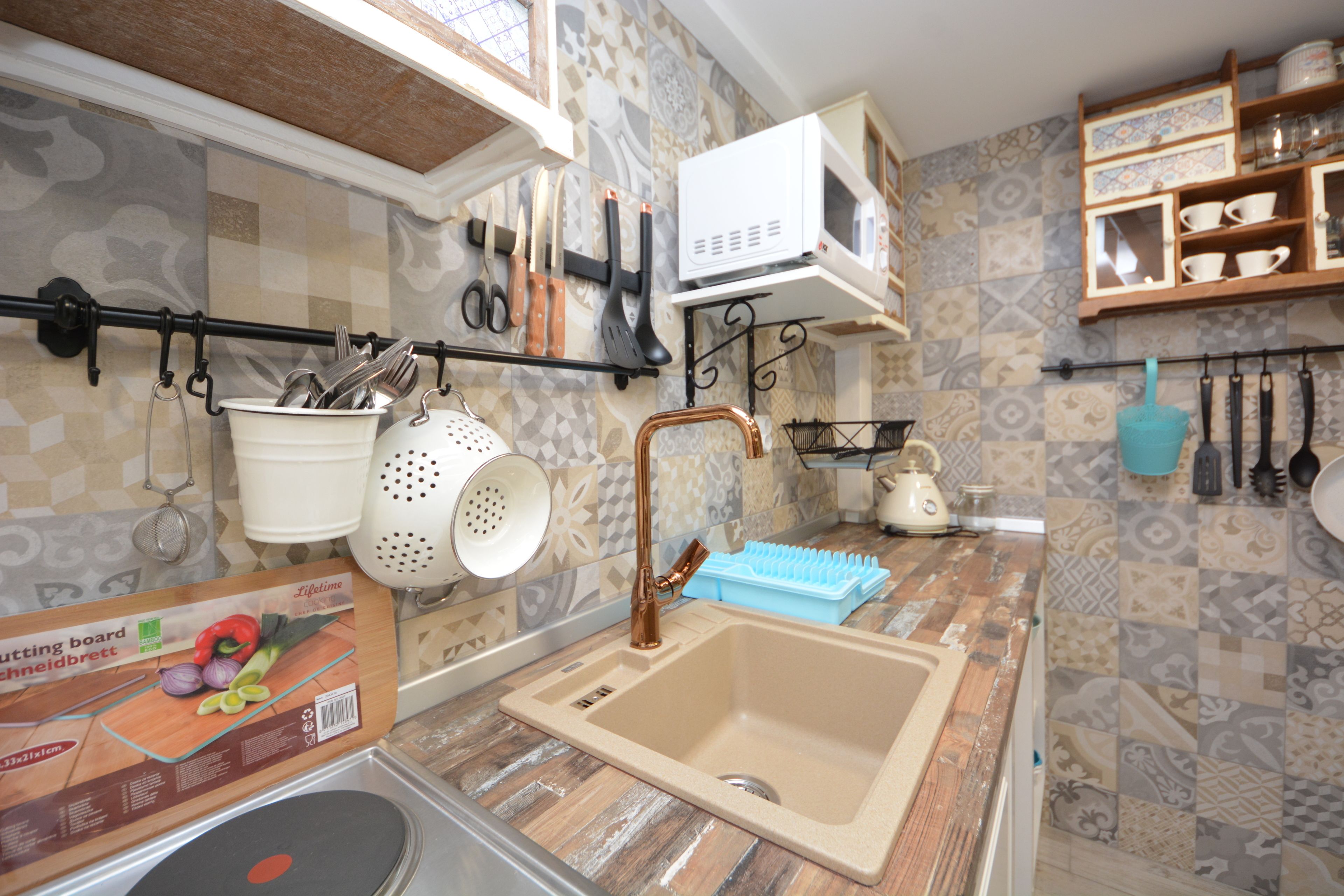A kitchen with a sink, a cutting board, and various utensils hanging on the wall.