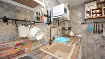 A kitchen with a sink, a cutting board, and various utensils hanging on the wall.