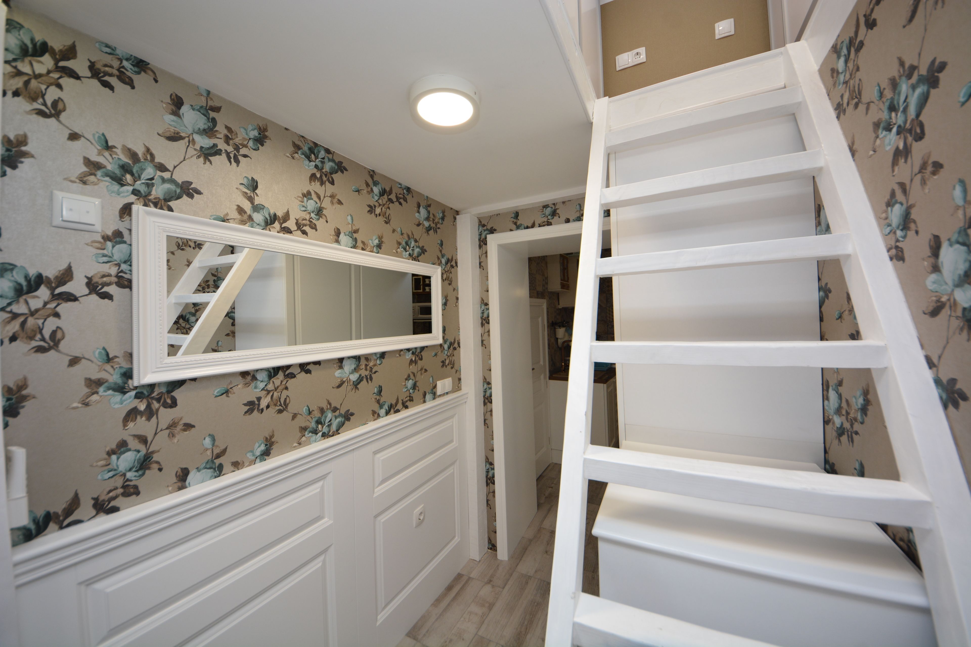 A hallway with floral wallpaper, a white wall-mounted mirror, and a white staircase.