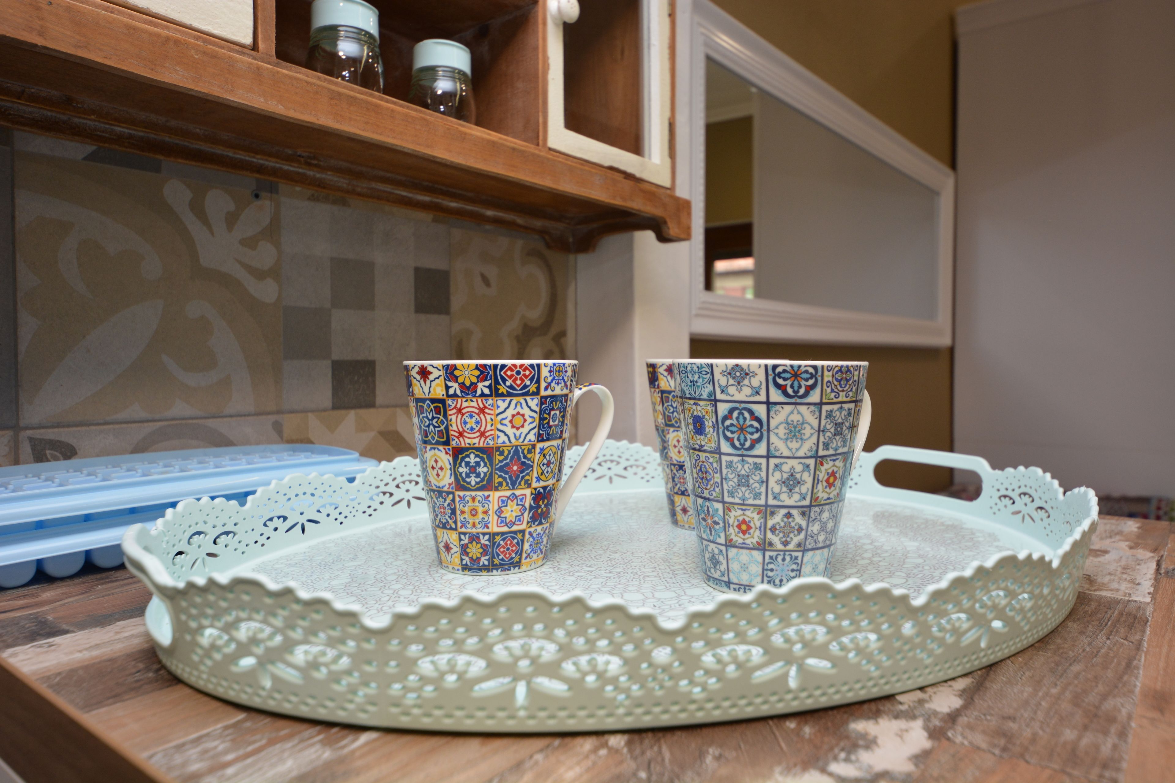 Two patterned cups on a tray, a blue silicone mold, and a decorative doily on a wooden surface.