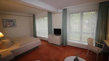 Habitación de hotel con cama, televisor, mesita con un florero, silla y escritorio.